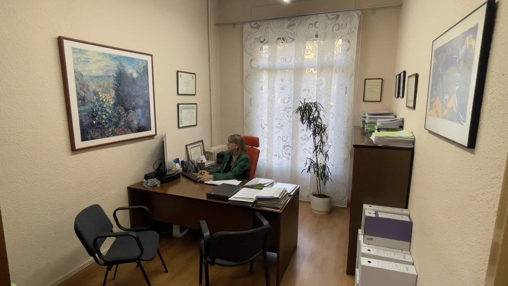 Asesora trabajando ante el ordenador en su despacho de la gestoría, con montones de documentos sobre la mesa