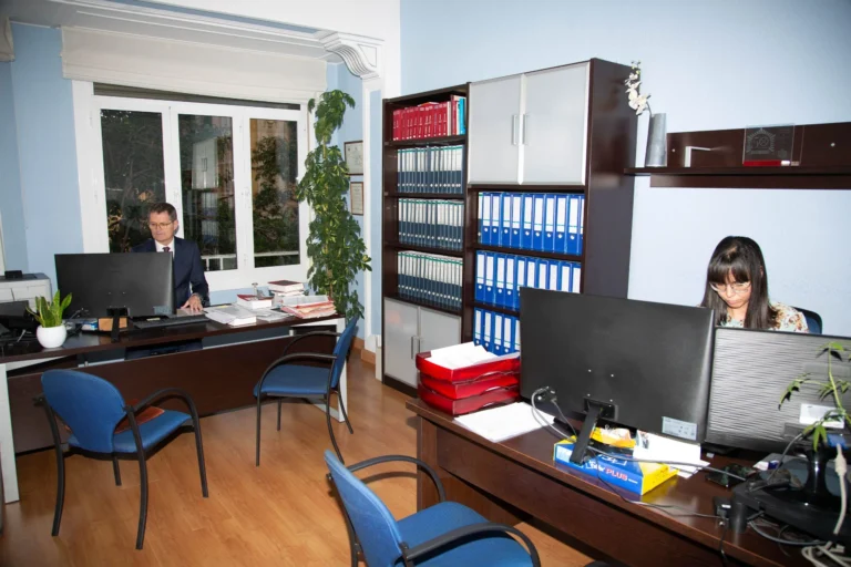 Despacho con archivadores azules, un asesor y una compañera al ordenador, donde se controla el absentismo laboral en Zaragoza