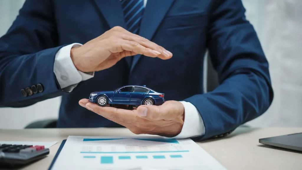 Hombre con traje protege con la mano un coche azul de juguete sobre un informe, bajas temporales de vehículos en Zaragoza