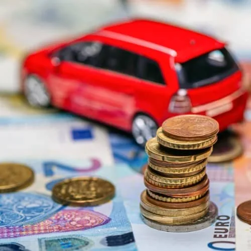 Coche rojo de juguete sobre billetes de euro y monedas, uno de los trámites que lleva una gestoría integral en Zaragoza