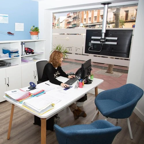 Asesora escribiendo al ordenador en una mesa con expedientes y sillas azules, en la gestoría para autónomos de Zaragoza