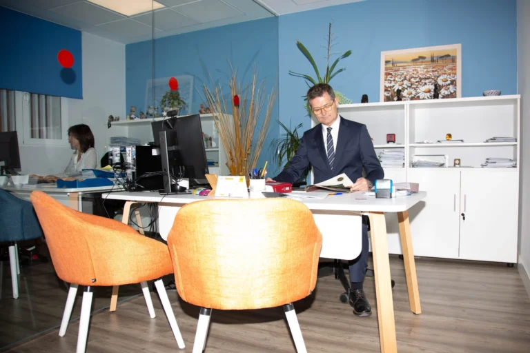 Asesor con traje lee unos papeles en su mesa con dos sillas naranjas delante, donde se calcula el IRPF en Zaragoza