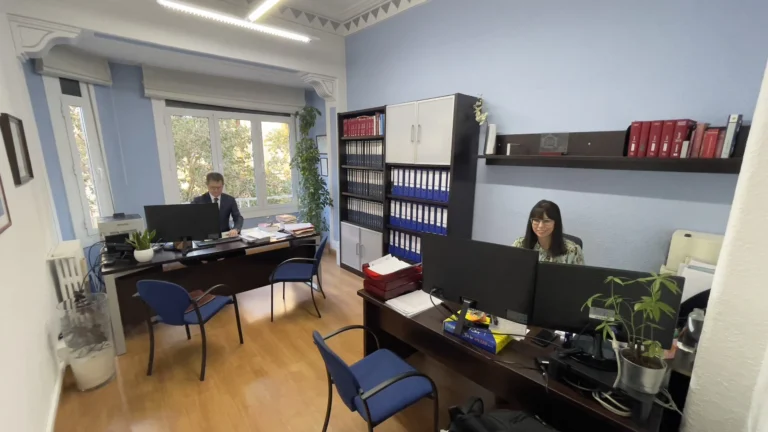 Despacho con archivadores azules y dos asesores trabajando al ordenador que preparan el modelo 190 en Zaragoza