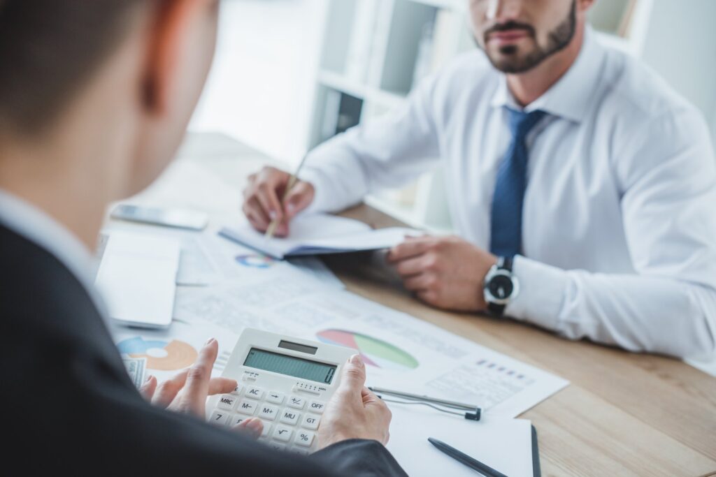Asesor calculando un presupuesto con la calculadora frente a un cliente que toma notas en la mesa de una oficina