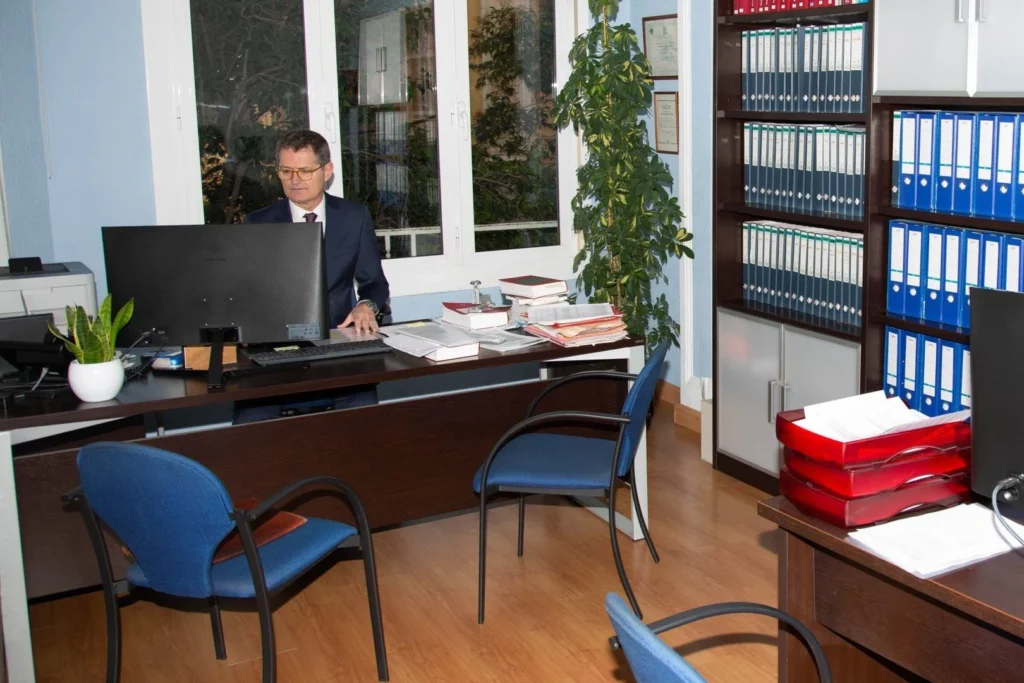 Asesor con traje al ordenador en su despacho con archivadores, con los papeles de un transportista autónomo en Zaragoza